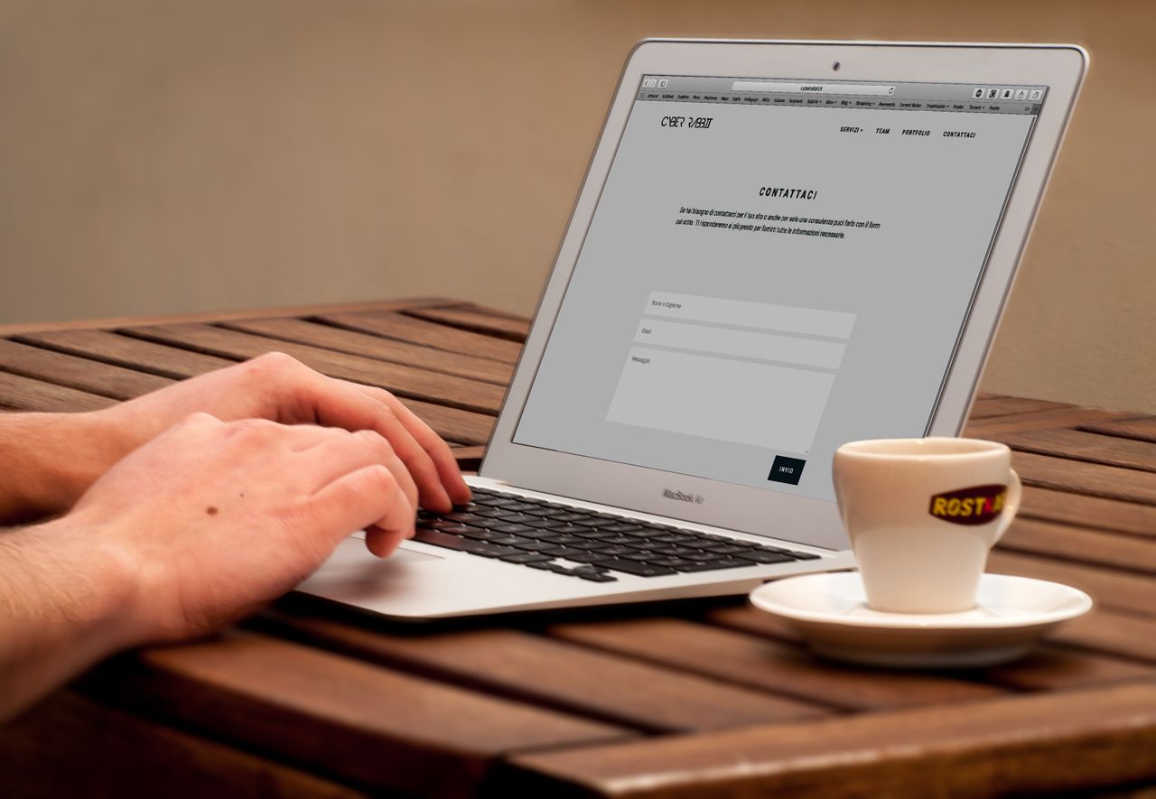 The Art of Drawing Readers In: Your attractive post title goes here Close-up of hands typing on a laptop next to a cup of coffee on a wooden desk.